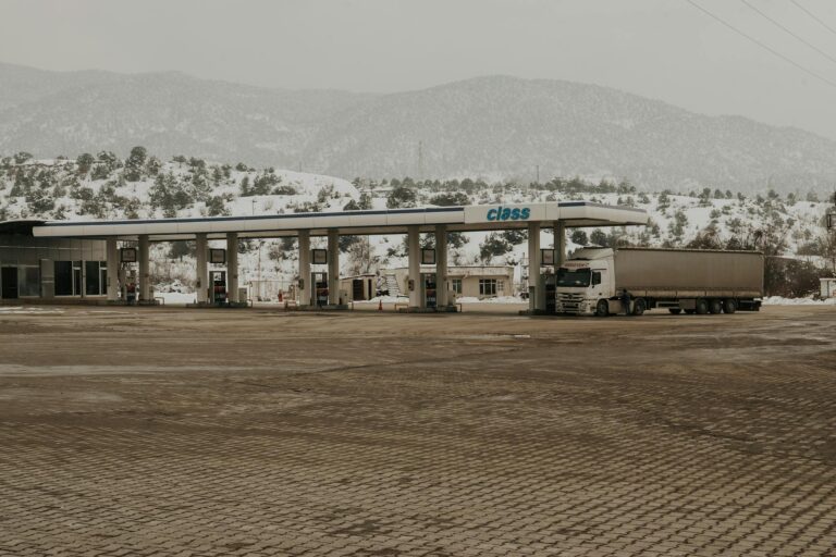 A snowy gas station with a truck and mountains in the backdrop, offering a serene winter scene.