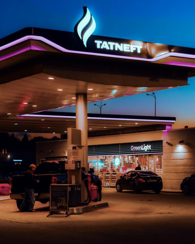 Gas station with vehicles at twilight, vibrant lighting, and recognizable brand.